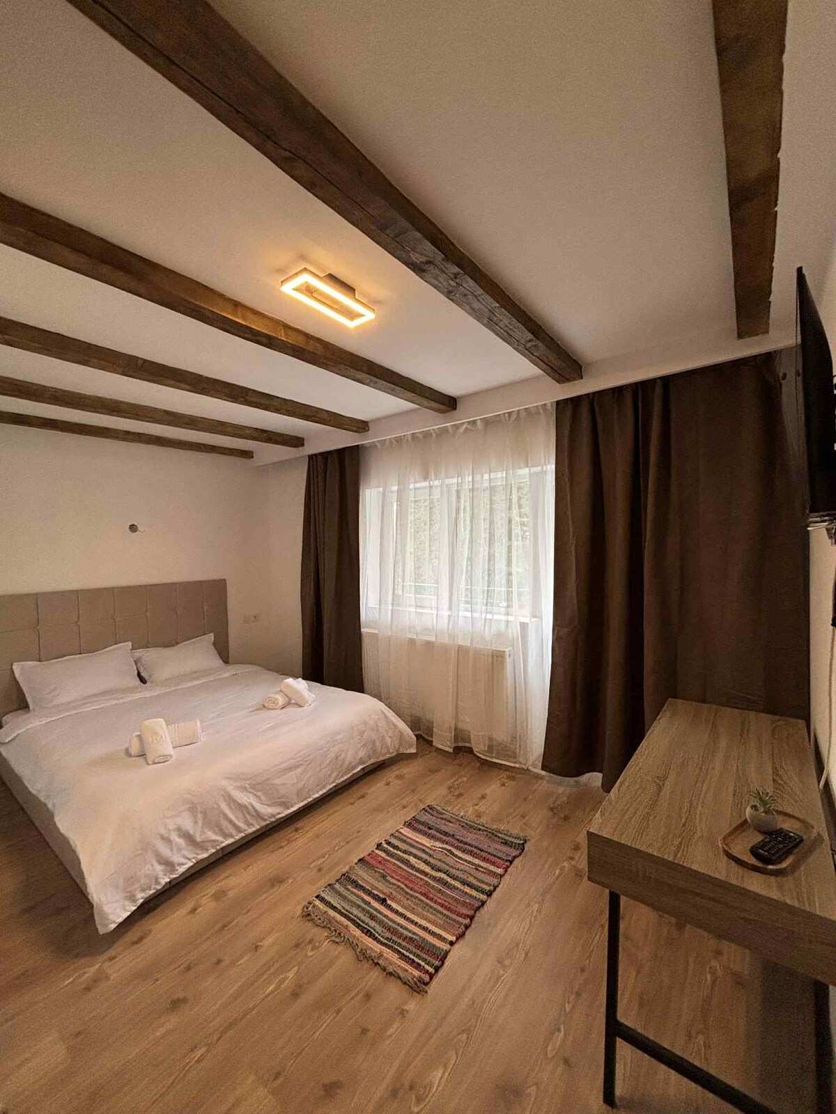 Room with a double bed, exposed wooden beams and curtains
